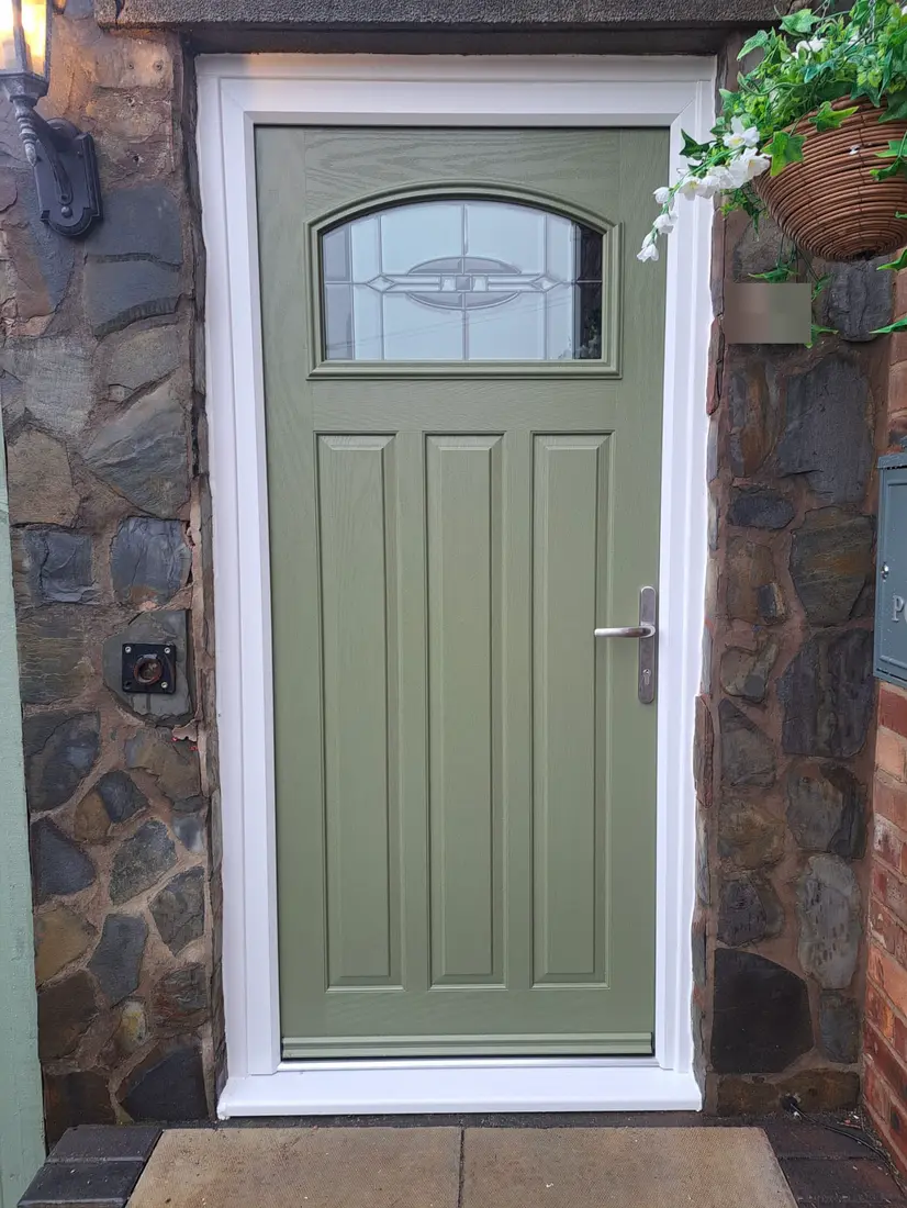 A green composite door with an arched glass panel in a stone wall